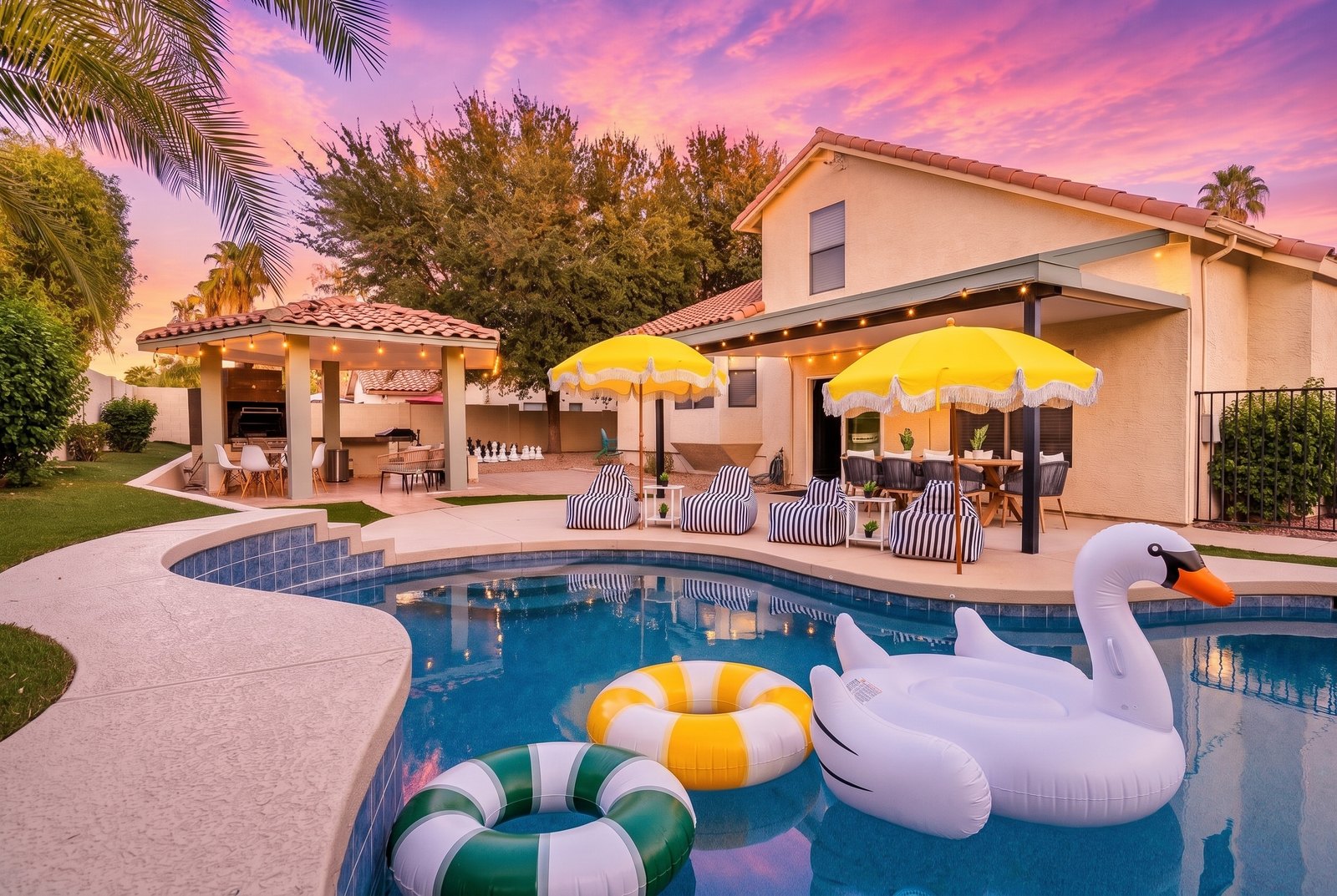 A home at dusk with a lit pool, shade umbrellas and a covered outdoor kitchen