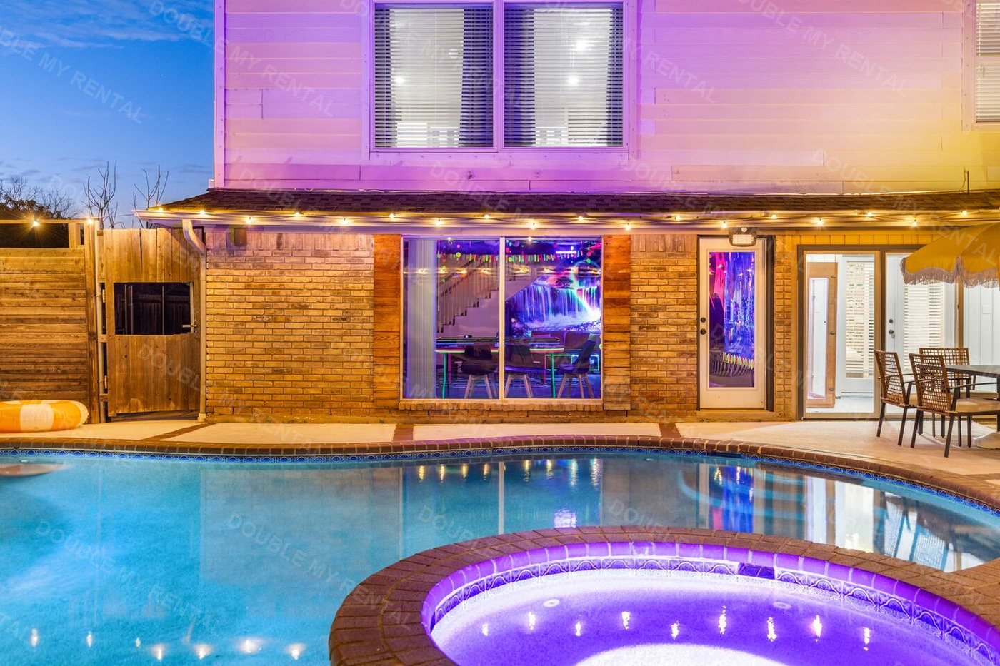 A private backyard pool and lit spa glowing at dusk behind the house